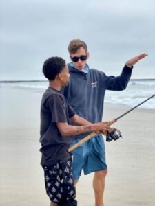 standing next to kids surf fishing at the beach